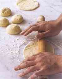 After the balls of dough have rested for 15 minutes, begin to roll them out by pressing them flat onto a floured surface with the palm of your hand (step 9)